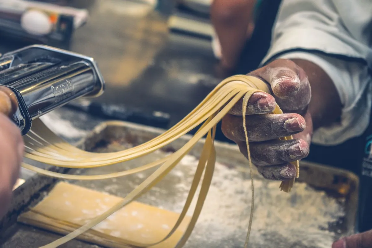 生パスタを手で扱う作業のイメージ。ハミングバードの製品や工場ではない